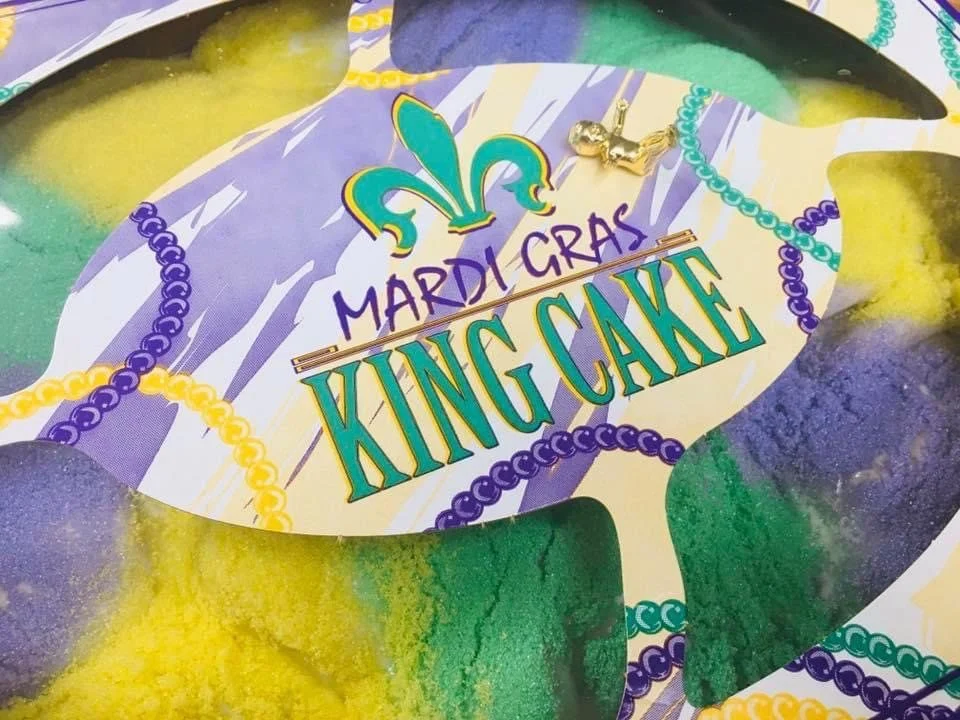 A Mardi Gras King Cake with purple, green and gold sugar, in its King Cake box